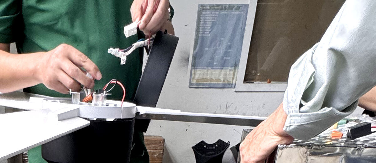 A technician wiring a ceiling fan motor and fitting a blade at the bench
